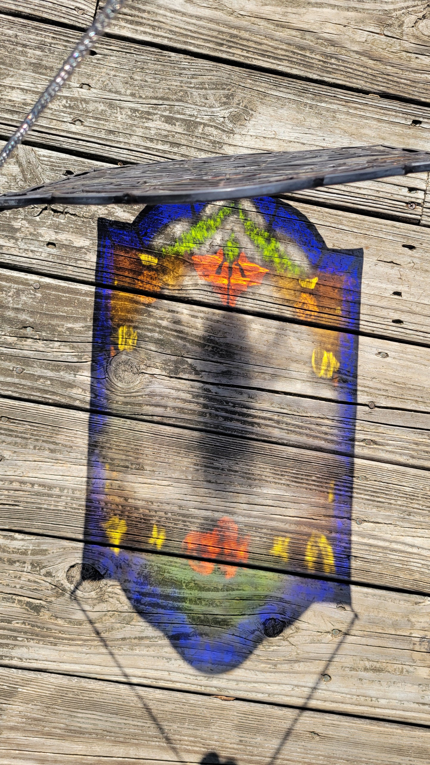 Colorful shadow reflection from a honeybee stained glass window panel cast onto a wooden deck in natural sunlight.