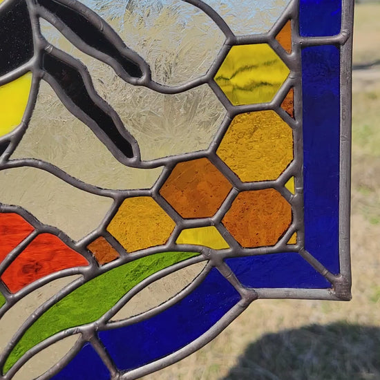 Honeybee stained glass window panel hanging in natural sunlight with vibrant blue, yellow, and orange glass details.